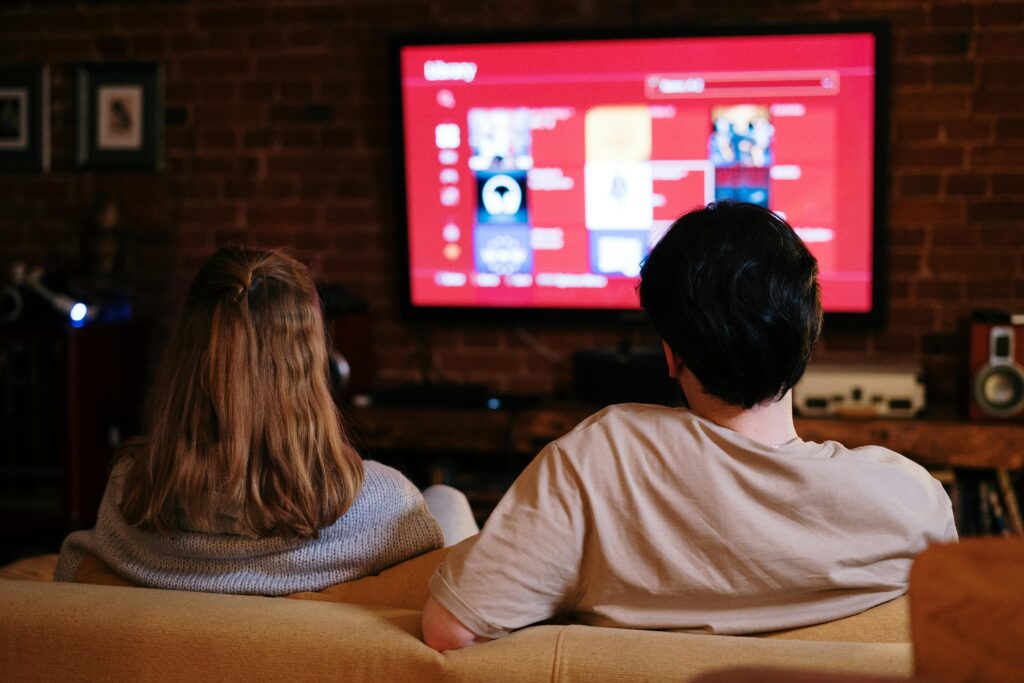 pexels-photo-4009409-4009409 A couple enjoys streaming shows on a large TV in a cozy, brick-walled living room.